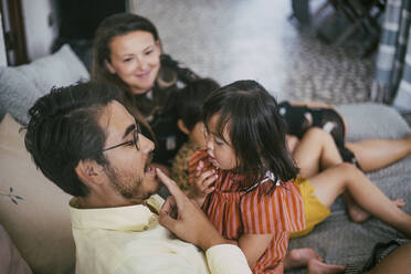 Father teaching daughter with disability while pointing at lips on sofa - MASF21095