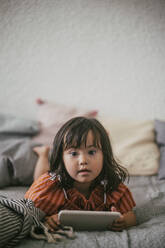 Portrait of down syndrome girl using digital tablet while lying on sofa at home - MASF21096