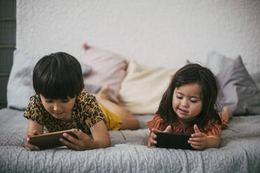 Lächelnde Down-Syndrom-Schwester und -Geschwister benutzen Smartphones, während sie zu Hause auf dem Sofa liegen - MASF21101
