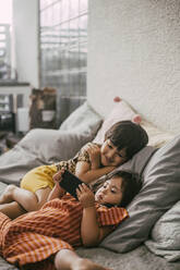 Down-Syndrom-Schwester benutzt Smartphone von Geschwisterkind, während sie zu Hause auf dem Sofa liegt - MASF21104