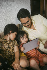 Down syndrome daughter using digital tablet by father and sister on sofa at home - MASF21105