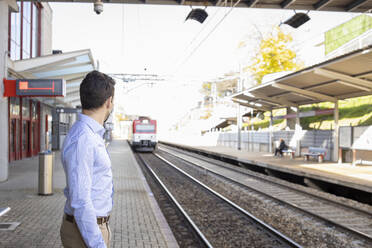 Geschäftsmann mit Gesichtsmaske wartet am Bahnsteig auf einen Zug - IFRF00210