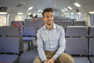 Lächelnder Geschäftsmann, der wegschaut, während er im Zug sitzt - IFRF00212