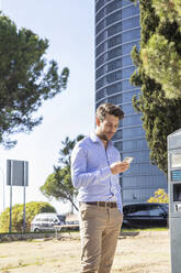 Businessman using smart phone while standing by parking meter in city - IFRF00224