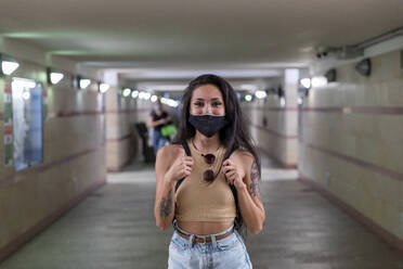 Junge Frau mit Schutzmaske, die eine Tasche trägt, während sie in einer unterirdischen Bahnhofspassage steht - WPEF03835