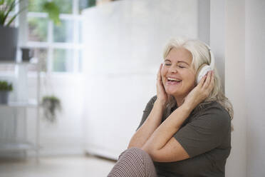 Glückliche ältere Frau, die in ihrer Wohnung Musik über Kopfhörer hört - JAHF00043
