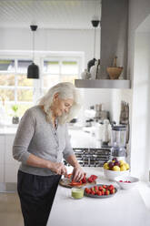 Retired senior woman cutting strawberries in kitchen at home - JAHF00050