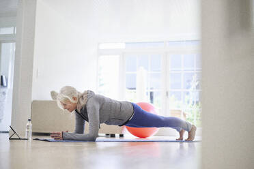 Active senior woman practicing plank position on mat at home - JAHF00066