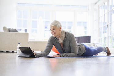 Smiling senior woman looking at digital tablet while e-learning exercises from digital tablet in apartment - JAHF00068