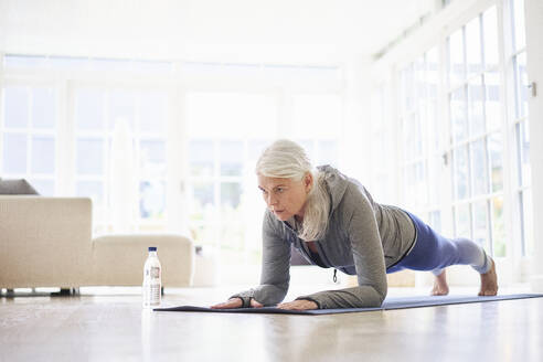 Retired active senior woman practicing plank position on mat at home - JAHF00069