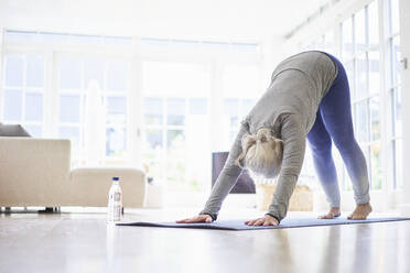 Active senior woman practicing yoga on mat in living room at apartment - JAHF00070