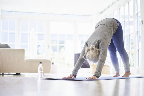 Aktive ältere Frau übt Yoga auf einer Matte im Wohnzimmer einer Wohnung - JAHF00070