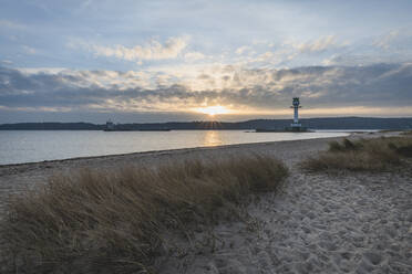 Deutschland, Schleswig-Holstein, Friedrichsort, Sandstrand bei Sonnenaufgang mit Leuchtturm im Hintergrund - KEBF01698