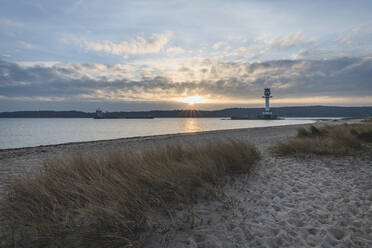 Germany, Schleswig-Holstein, Friedrichsort, Sandy coastal beach at sunrise with lighthouse in background - KEBF01698