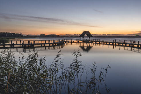 Deutschland, Schleswig-Holstein, Hemmelsdorf, Silhouette der leeren Seebrücke am Ufer des Hemmelsdorfer Sees in der Morgendämmerung - KEBF01711