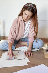 Woman making charcoal drawing on paper in living room - VEGF03344