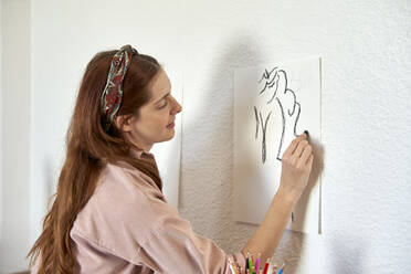 Lächelnde Künstlerin, die mit Kohle auf Papier zeichnet und zu Hause an die Wand klebt - VEGF03345