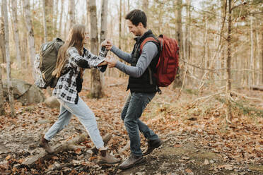 Junger Mann hilft seiner Freundin bei einer Wanderung im Herbstwald - SMSF00482