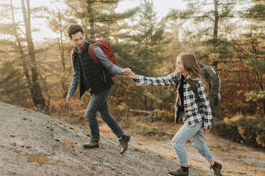 Young couple holding hands while walking up hill during autumn hike - SMSF00489