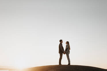 Young couple holding hands against clear sky at sunset - SMSF00507