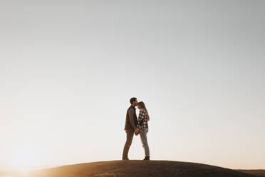 Junges Paar hält Hände gegen klaren Himmel bei Sonnenuntergang - SMSF00508
