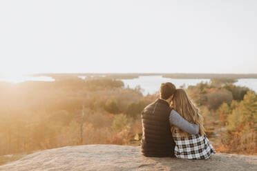 Junges Paar sitzt zusammen auf einem Felsen und bewundert die untergehende Sonne im Herbst - SMSF00510