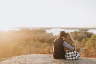 Young couple sitting together on rocky surface admiring setting sun in autumn - SMSF00510