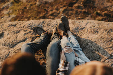 Legs of young couple sitting together on rocky surface - SMSF00511