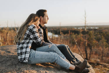 Junges Paar sitzt bei einer Herbstwanderung auf einem Felsen zusammen - SMSF00512