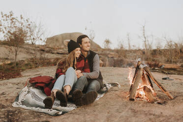 Junges Paar sitzt zusammen vor einem Lagerfeuer - SMSF00524