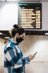 Mann mit Gesichtsschutz, der ein Mobiltelefon benutzt, während er in einer U-Bahn-Station steht - EBBF01895
