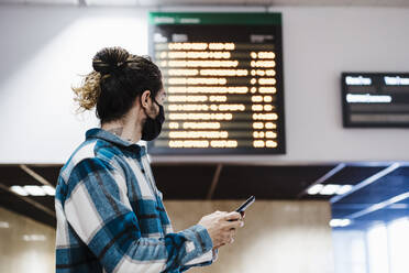 Junger Mann mit Gesichtsmaske, der ein Mobiltelefon benutzt, während er in einer U-Bahn-Station wartet - EBBF01896