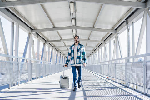 Junger Mann geht mit Gepäck auf einer Brücke, lizenzfreies Stockfoto