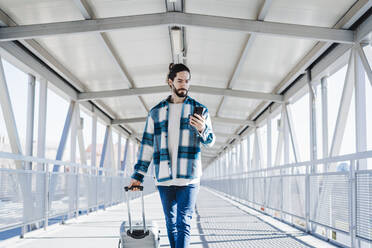 Mann benutzt Mobiltelefon, während er mit Gepäck auf einer Brücke geht - EBBF01908