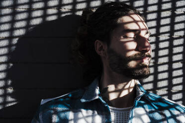 Man with eyes closed and shadow on face leaning on wall - EBBF01912