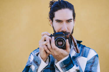 Tourist standing with camera against yellow wall - EBBF01915