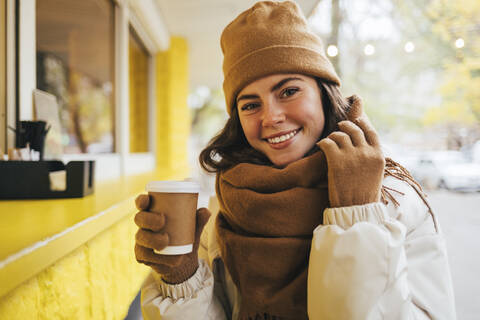 Lächelnde Frau mit Schal und Einweg-Kaffeetasse in einem Straßencafé im Herbst, lizenzfreies Stockfoto