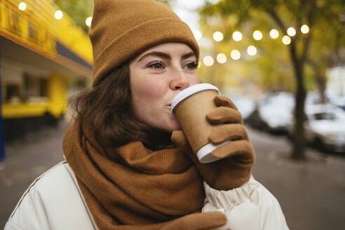 Junge Frau in warmer Kleidung trinkt Kaffee auf der Straße im Herbst - OYF00306