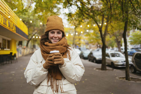 Glückliche Frau mit Einweg-Kaffeebecher auf dem Gehweg im Herbst - OYF00310
