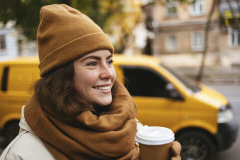 Lächelnde junge Frau mit Einweg-Kaffeetasse im Winter, lizenzfreies Stockfoto