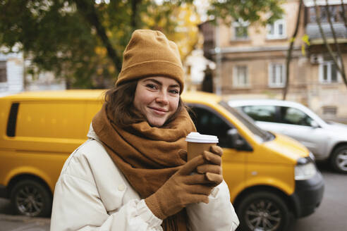 Lächelnde Frau mit Einweg-Kaffeebecher auf dem Gehweg im Winter - OYF00313