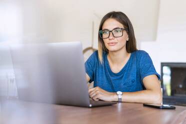 Geschäftsfrau mit Brille, die im Heimbüro auf einen Laptop schaut - SBOF02290