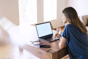 Brünette Geschäftsfrau mit Laptop am Tisch bei der Arbeit im Heimbüro - SBOF02294