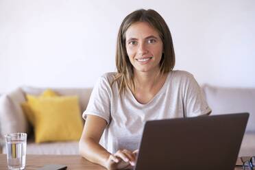 Lächelnde weibliche Fachkraft, die einen Laptop bei der Arbeit zu Hause benutzt - SBOF02296