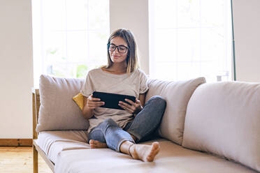 Entspannte brünette Geschäftsfrau, die auf dem Sofa sitzt und ein digitales Tablet im Wohnzimmer zu Hause benutzt - SBOF02299