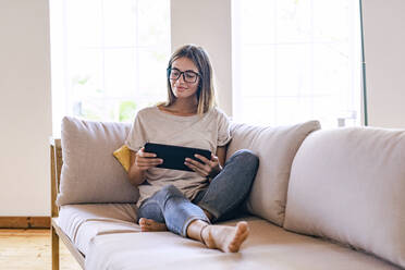 Relaxed brunette businesswoman sitting on sofa while using digital tablet in living room at home - SBOF02299