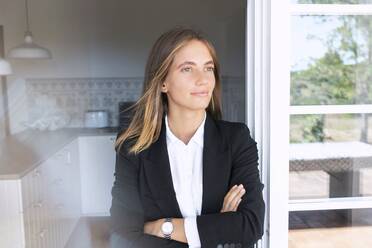 Thoughtful young businesswoman with arms crossed leaning on door while looking away - SBOF02302