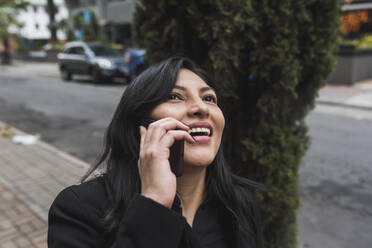 Glückliche Frau, die in der Stadt mit einem Smartphone telefoniert - DSIF00256