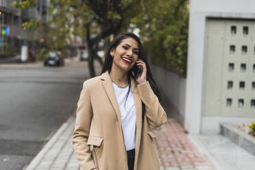 Attractive woman talking over smart phone while standing on footpath in city - DSIF00261