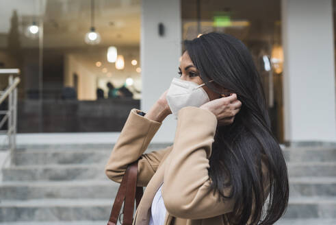 Woman wearing protective face mask standing by steps outside building during COVID-19 - DSIF00262
